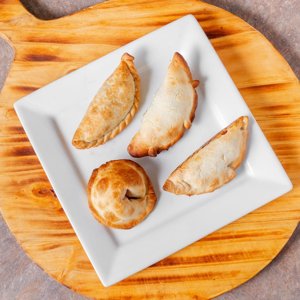 Four golden-brown empanadas, two crescent-shaped and two round, on a white rectangular plate.