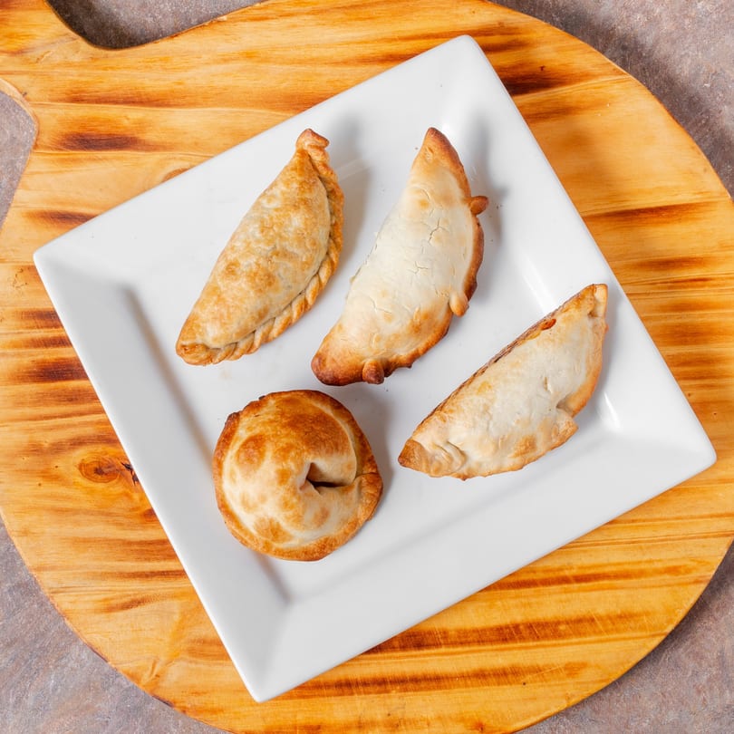 Four golden-brown empanadas, two crescent-shaped and two round, on a white rectangular plate.
