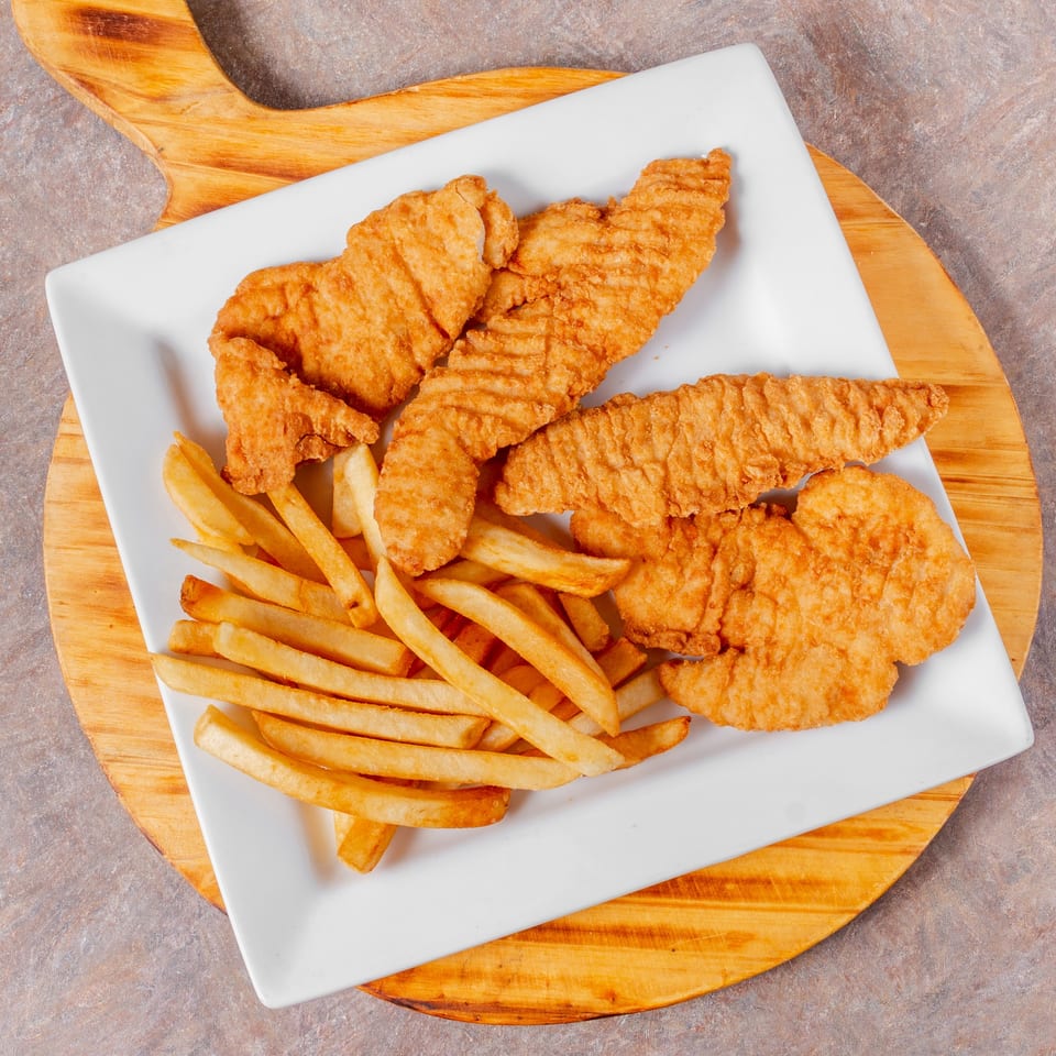 Crispy fried chicken tenders and golden french fries on a white rectangular plate, on a wooden board.