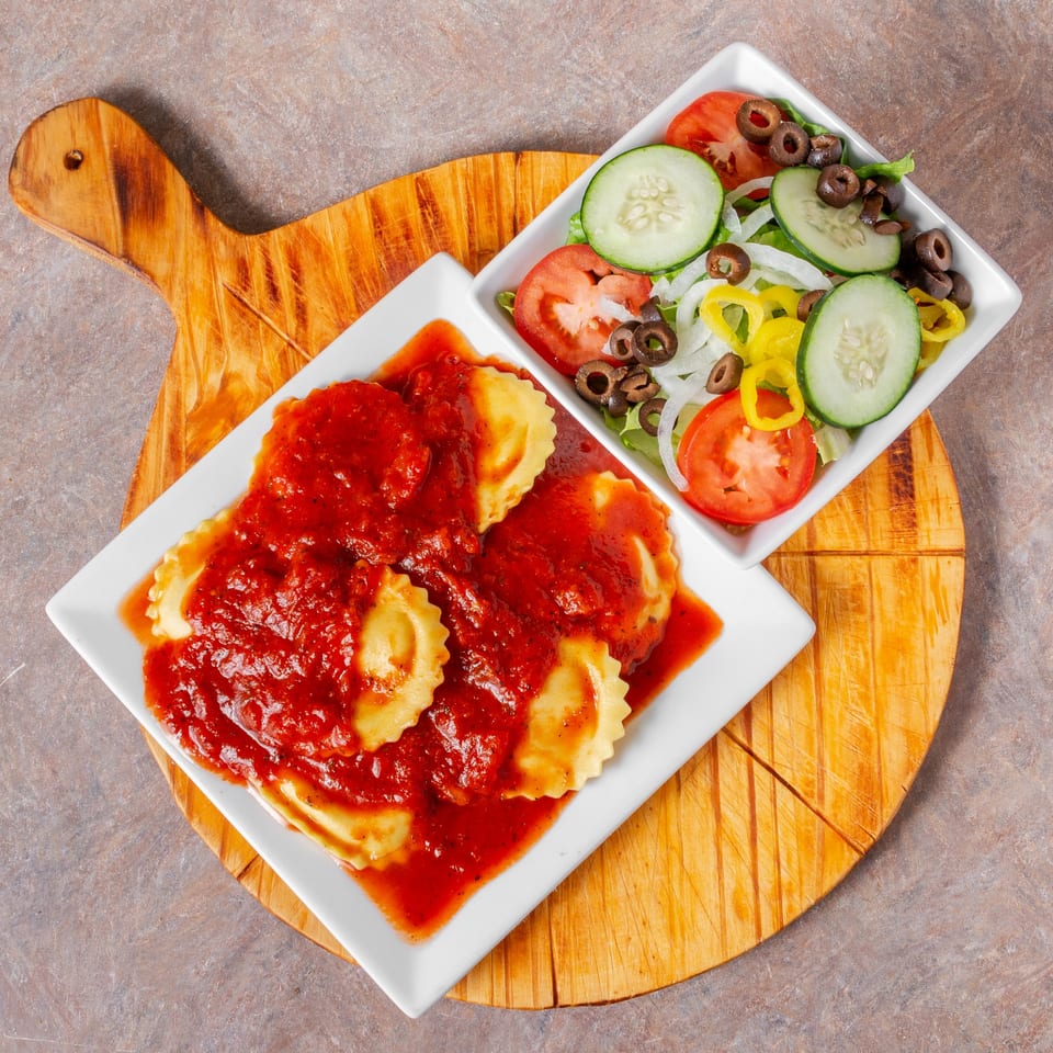 Ravioli with red sauce and a side salad with cucumbers, tomatoes, olives, and peppers.