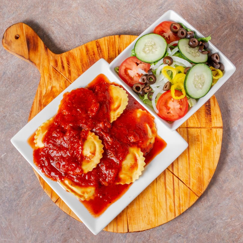 Ravioli with red sauce and a side salad with cucumbers, tomatoes, olives, and peppers.